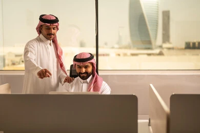 Focus and meticulous work, explaining and sharing experiences among colleagues, dialogues and discussions within the team, business and company development, work meetings and project completion, discussing plans and explaining work tasks, Arab Saudi Gulf colleagues wearing traditional attire and shemagh exchanging conversation.