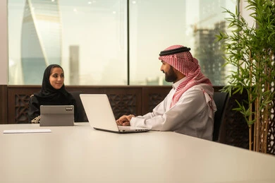 Arab Saudi Gulf colleagues in a meeting, Saudi employees using laptops and tablets, business and company development, work meeting and project completion, focus and meticulous work, dialogues and discussions within the team, discussing plans and explaining work tasks.