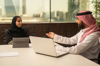 Discussion of plans and explanation of work tasks, business and company development, work meetings and project completion, focus and meticulous work, dialogues and discussions within the team, Arab Saudi Gulf colleagues in a meeting, Saudi employees using laptops and tablets.