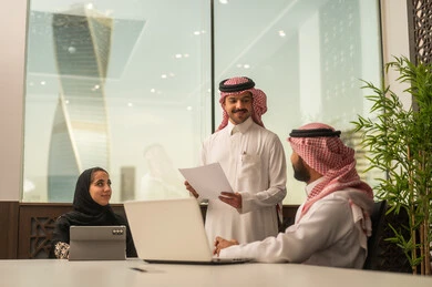 Focus and meticulous work, business and company development, work meetings and project completion, dialogues and discussions within the team, discussing plans and explaining work tasks, Arab Saudi Gulf colleagues in a meeting, Saudi employees using laptops and tablets.