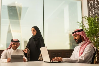 Focus and meticulous work, business and company development, work meetings and project completion, dialogues and discussions within the team, discussing plans and explaining work tasks, Arab Saudi Gulf colleagues in a meeting, Saudi employees using laptops and tablets.