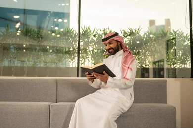 الاستمتاع باوقات الفراغ ، ثقافة التعلم الذاتي، قراءة الكتب بتمعن ، رجل عربي خليجي سعودي مبتسم يرتدي الثوب التقليدي والشماغ يحمل بيده كتاب تثقيفي ، إيماءات التركيز والاندماج ، قراءة الروايات والقصص .
