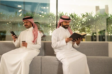 موظفين عربيين خليجيين سعوديين يجلسون داخل المكتب ، العمل في الشركات السعودية الراقية, العمل على الهاتف المحمول ، مناقشة المشاريع ومتابعة إستراتيجية العمل، الاستمتاع بالمشروبات الساخنه ، القراءه وحب المطالعه