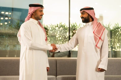 الاتفاق والشراكة على الأعمال والمشاريع التجارية، تعارف وصداقات وبناء علاقات اجتماعية، صفقات عمل جديدة ناجحة بين رجال الأعمال، رجلان عربيان خليجيان سعوديان يرتديان الزى التقليدي والشماغ يقومان بمصافحة بعضهما داخل مقر الشركة بإيماءات السعادة والسرور