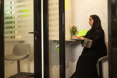 Working in offices and companies, online business meetings and completing projects, focus and meticulous work, dialogues and discussions within the team, business and company development, discussing plans and explaining work tasks, an Arab Gulf Saudi female employee wearing an abaya and hijab using a laptop.