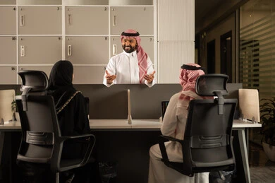 Work meeting and project completion, designated spaces for each employee in the company, focus and meticulous work, dialogues and discussions within the team, business and company development, discussing plans and explaining work tasks, Arab Saudi Gulf colleagues using laptops.