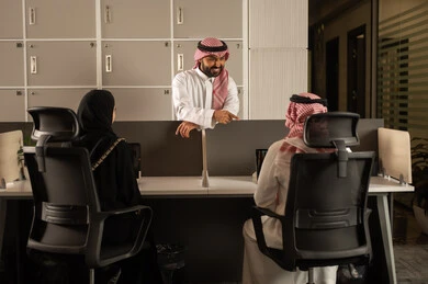Conversations and discussions within the team, designated spaces for each employee in the company, focus and meticulous work, business and company development, work meetings and project completion, discussing plans and explaining job tasks, Arab Saudi Gulf colleagues using laptops.