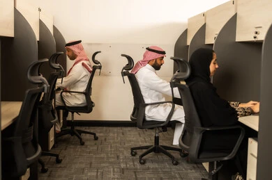 Designated spaces for each employee in the company, focus and meticulous work, dialogues and discussions within the team, business and company development, work meetings and project completion, discussing plans and explaining job tasks, Arab Saudi Gulf colleagues using laptops.