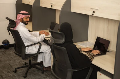 Designated spaces for each employee in the company, focus and meticulous work, dialogues and discussions within the team, business and company development, work meetings and project completion, discussing plans and explaining job tasks, Arab Saudi Gulf colleagues using laptops.