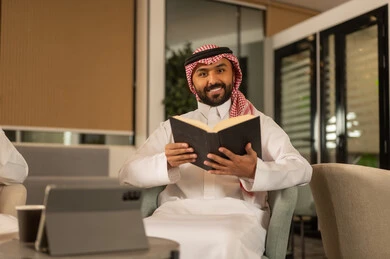 الاستمتاع باوقات الفراغ ، ثقافة التعلم الذاتي، قراءة الكتب بتمعن ، رجل عربي خليجي سعودي مبتسم يرتدي الثوب التقليدي والشماغ يحمل بيده كتاب تثقيفي ، إيماءات التركيز والاندماج ، قراءة الروايات والقصص .
