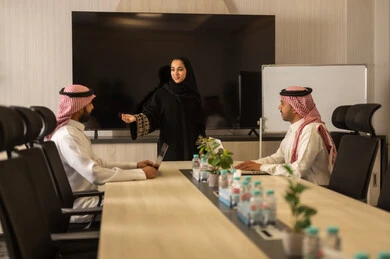 Collaboration and understanding among the team, exchanging experiences and successful agreements, organizing and managing work objectives, a comfortable work environment, Saudi employees using laptops, happily explaining the required tasks, Arab Saudi Gulf colleagues in a meeting to study the project and objectives in detail.