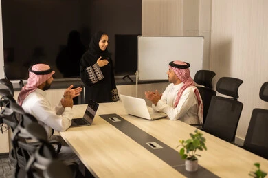 Collaboration and understanding among the team, exchanging experiences and successful agreements, organizing and managing work objectives, a comfortable work environment, Saudi employees using laptops, happily explaining the required tasks, Arab Saudi Gulf colleagues in a meeting to study the project and objectives in detail.