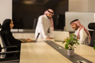 Organizing and managing work objectives, cooperation and understanding among the team, exchanging experiences and successful agreements, a comfortable work environment, Saudi employees using laptops, happily explaining the required tasks, Arab Saudi Gulf colleagues in a meeting to study the project and objectives accurately.