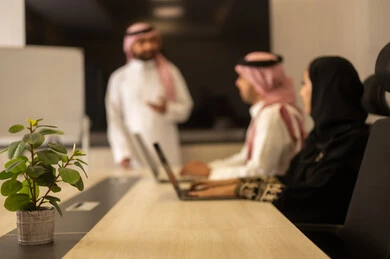 Exchange of experiences and successful agreements, organizing and managing work objectives, cooperation and understanding among the team, a comfortable work environment, Saudi employees using laptops, happily explaining the required tasks, Arab Saudi Gulf colleagues in a meeting to study the project and objectives in detail.