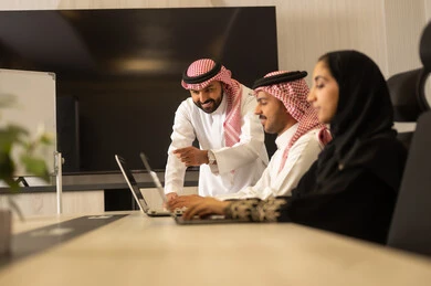 Saudi employees are using laptops and tablets, developing businesses and companies, holding work meetings and completing projects, focusing and working meticulously, engaging in dialogues and discussions within the team, discussing plans and explaining work tasks, Arab Saudi Gulf colleagues in a meeting.