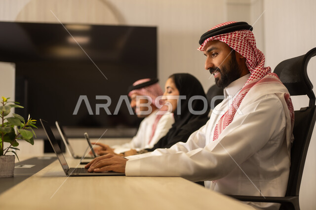 Discussion of plans and explanation of work tasks, business and company development, work meetings and project completion, focus and meticulous work, dialogues and discussions within the team, Arab Saudi Gulf colleagues in a meeting, Saudi employees using laptops and tablets.