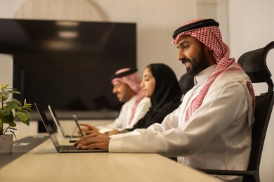 Discussion of plans and explanation of work tasks, business and company development, work meetings and project completion, focus and meticulous work, dialogues and discussions within the team, Arab Saudi Gulf colleagues in a meeting, Saudi employees using laptops and tablets.