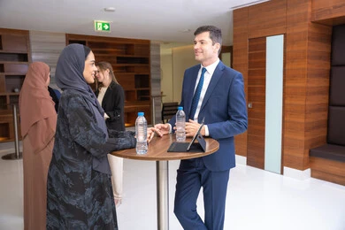 Teamwork and team spirit, closing new deals, strategic planning and organization to achieve goals, networking and building social relationships, an Arab Gulf Emirati woman discussing work methods and professional development with a foreign businessman, holding a meeting inside the company headquarters, background of businessmen.