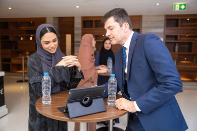 Using technology with daily tasks, closing new deals, strategic planning and organization to achieve goals, networking and building social relationships, an Arab Gulf Emirati woman discusses work methods and professional development with a foreign businessman, holding a meeting inside the company headquarters, background of businessmen. Using technology with daily tasks, closing new deals, strategic planning and organization to achieve goals, networking and building social relationships, an Arab Gulf Emirati woman discusses work methods and professional development with a foreign businessman, holding a meeting inside the company headquarters, background of businessmen.