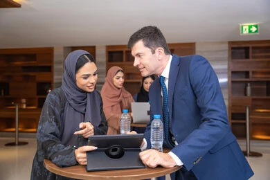 الجهاز اللوحي مع المهام اليومية، عقد الصفقات الجديدة ،التخطيط الاستراتيجي والتنظيم لتحقيق الأهداف، التعارف وبناء العلاقات الاجتماعية، سيدة عربية خليجية اماراتية تناقش اساليب العمل والتطوير المهني مع سيد اعمال اجنبية، عقد اجتماع داخل مقر الشركة، خلفية رجال اعمال