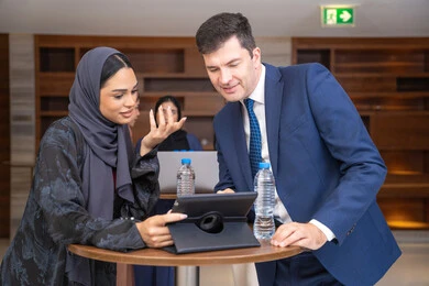 استعمال الجهاز اللوحي مع المهام اليومية، عقد الصفقات الجديدة ،التخطيط الاستراتيجي والتنظيم لتحقيق الأهداف، التعارف وبناء العلاقات الاجتماعية، سيدة عربية خليجية اماراتية تناقش اساليب العمل والتطوير المهني مع سيد اعمال اجنبية، عقد اجتماع داخل مقر الشركة، خلفية رجال اعمال