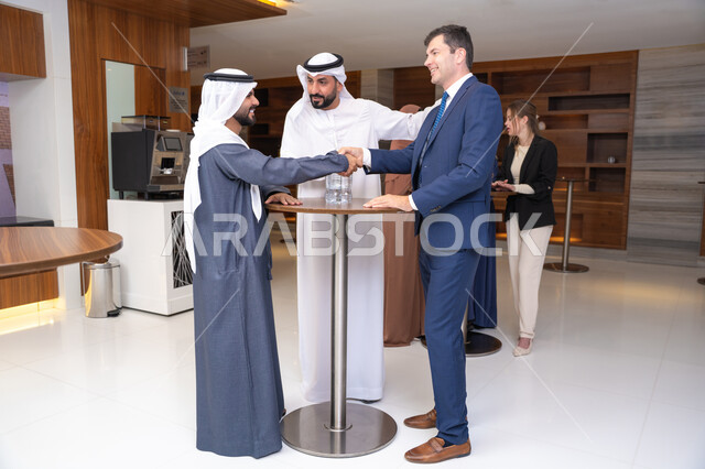Welcoming and getting to know a new guest, discussion and understanding among employees, exchanging experiences and information to achieve goals, strategic planning and organization to achieve objectives, concluding new deals, a group of Arab Gulf Emirati men discussing work methods and professional development with a foreign businessman.