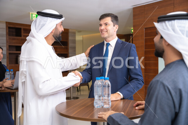 Partnership and cooperation in accomplishing tasks, discussion and understanding among employees, exchanging experiences and information to achieve goals, strategic planning and organization, concluding new deals, a group of Arab Gulf Emirati men discussing work methods and professional development with a foreign businesswoman.