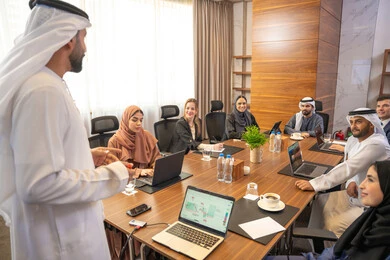 Using a laptop, following up on work tasks, discussion and understanding among employees, strategic plans to achieve goals, holding a meeting within the company, office professions and jobs, an Arab Gulf Emirati man explaining work methods and professional development to a group of Arab and foreign individuals.