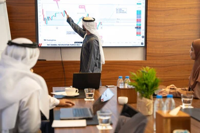 Using a display screen to confirm understanding, discussion, and communication among employees, strategic plans to achieve goals, holding a meeting within the company, office professions and jobs, an Arab Gulf Emirati man explaining work methods and professional development to a group of Arab and foreign individuals.