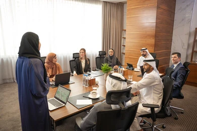The spirit of teamwork, women's professions and jobs, using a display screen for clearer explanations, ensuring a clear and comprehensive understanding of the work, discussion and understanding among employees, strategic plans to achieve goals, an Arab Gulf Emirati woman explaining work methods and professional development to a group of Arab and foreign individuals.