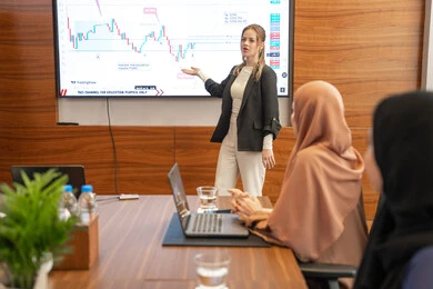 Cultural exchange between different companies, dialogue and understanding among employees, unity and teamwork, professions and office jobs, using a display screen for clearer explanations, ensuring a clear and comprehensive understanding of the work, strategic plans to achieve goals, a foreign businessman discussing work methods and professional development within an Emirati company.