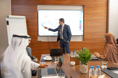 Teamwork and team spirit, dialogue and understanding among employees, unity and collaboration, office professions and jobs, using a display screen for clearer explanations, ensuring a clear and comprehensive understanding of the work, strategic plans to achieve goals, a foreign businessman discussing work methods and professional development within an Emirati company.