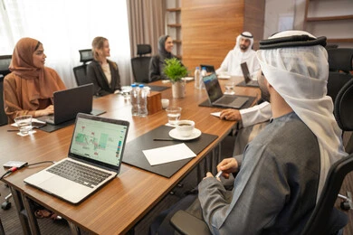 Completing work tasks through a laptop, an Emirati work environment, studying and analyzing new projects, dialogue and understanding among employees, unity and teamwork, office professions and jobs, ensuring a clear and comprehensive understanding of business, a foreign businessman in a business meeting inside an Emirati company with an Emirati Arab man.