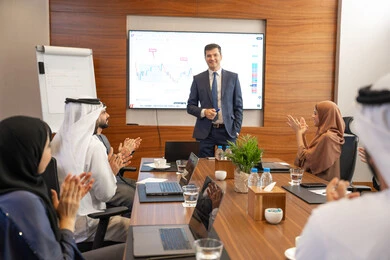 Company goals and policies, Emirati work environment, dialogue and understanding among employees, unity and teamwork, professions and office jobs, using a display screen for clearer explanations, ensuring a clear and comprehensive understanding of the work, a foreign businessman discussing work methods and professional development within an Emirati company.