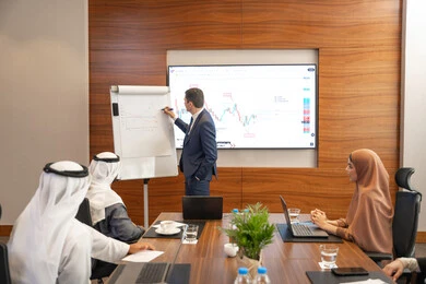 Consolidating information through writing on the board, new partnership deals, an Emirati work environment, dialogue and understanding among employees, unity and teamwork, office professions and jobs, ensuring a clear and comprehensive understanding of business, a foreign businessman discussing work methods and professional development within an Emirati company.