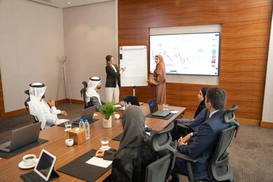 Discussion of work matters using papers and data, new partnership deals, Emirati work environment, dialogue and understanding among employees, unity and teamwork, office professions and jobs, ensuring a clear and comprehensive understanding of business, a foreign businesswoman discussing work methods and professional development with an Emirati woman.