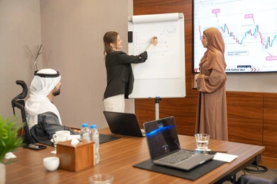 Study and analysis of new projects, new partnership deals, Emirati work environment, dialogue and understanding among employees, unity and teamwork, office professions and jobs, ensuring a clear and comprehensive understanding of business, a foreign businesswoman discussing work methods and professional development with an Emirati woman.