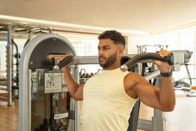 تقوية العضلات والاعصاب, التدرب بعزيمة للمحافظة على نظام الحياة الصحي, اهمية الرياضة لبناء جسد قوي, زيادة المرونة و القوة, رجل عربي خليجي إماراتي يرتدي الملابس الرياضية و يتمرن على آلة تمرين الأكتاف, بناء الكتلة العضلية