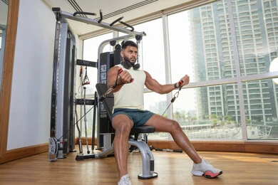 بناء الكتلة العضلية، تقوية العضلات والاعصاب، مفهوم الرشاقة واللياقة البدنية، رجل عربي خليجي إماراتي يرتدي الملابس الرياضية يتمرن على آلة تمرين عضلات الصدر و يضع سماعه الرأس حول رقبته, اتباع أسلوب حياة صحي, استخدام الأجهزة الرياضية