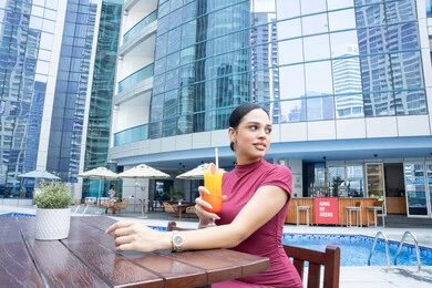Attention to style and outward appearance, the concept of softness and femininity, enjoying refreshing cold drinks, relaxing outdoors, a young Emirati Gulf Arab woman wearing casual clothes and drinking a fresh beverage, the joy of spending time with oneself