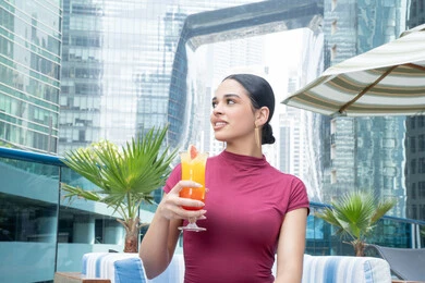 Confident gestures, enjoying favorite drinks, paying attention to style and appearance, the concept of softness and femininity, relaxing outdoors, a smiling young Emirati woman from the Gulf wearing casual clothes, the joy of spending time with oneself