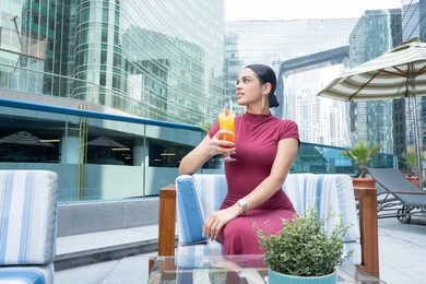 مفهوم النعومة والأنوثة, الاهتمام بالأناقة والمظهر الخارجي, الاستمتاع بالمشروبات الباردة المنعشة, الاسترخاء في الهواء الطلق, شابة عربية خليجية اماراتية ترتدي الزي الكاجوال و تشرب مشروب طازج, متعة قضاء الوقت مع الذات