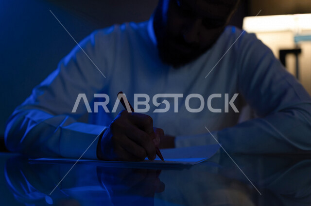 رجل عربي خليجي سعودي يمسك بيده قلم، كاتب وروائي، تحليل الافكار والمشاريع، مشروع عمل جديد، سكرتير يدير الاعمال الورقية، أعمال مكتبية
