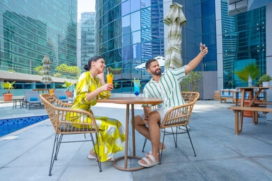 Enjoying drinks outside the home, documenting family moments, taking memorable selfies on their mobile phones, engaging in fun recreational activities, an Emirati Gulf Arab couple in casual attire sitting at a resort in the UAE