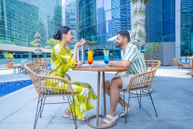 ايماءات السرور و الاندماج, أنشطة عائلية ترفيهيه، محاولة التخفيف من حرارة الصيف بالمشروبات المنعشة، الإستجمام في الهواء الطلق, قضاء الأوقات المسلية, القيام بالأنشطة الممتعة في الإجازة, زوجان عربيان خليجيان إماراتيان يرتديان الزي الكاجوال يجلسان في إحدى المنتجعات في الإمارات