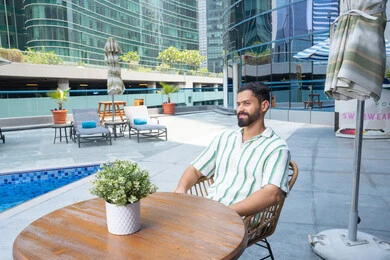The concept of comfort and relaxation, enjoying a tranquil atmosphere, a smiling Emirati Gulf Arab man in casual attire sitting by the pool, engaging in enjoyable holiday activities, spending entertaining time, gestures of joy and happiness