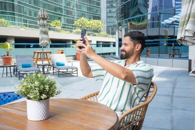 ايماءات وجه سعيدة، الاستمتاع باجواء هادئه خارج المنزل, الهروب من حرارة الصيف، مفهوم الاستجمام والاختلاء, الاسترخاء في الهواء الطلق, رجل عربي خليجي اماراتي يرتدي الزي الكاجوال و يقوم بالتقاط صور سيلفي للتذكار, القيام بالأنشطة الممتعة في الإجازة