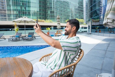 Enjoying a peaceful atmosphere outdoors, escaping the summer heat, the concept of relaxation and seclusion, unwinding in the open air, an Emirati Gulf Arab man wearing casual clothes and taking selfies as a souvenir, engaging in fun activities during the holiday