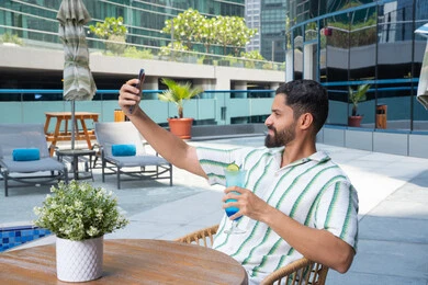 مفهوم الاستجمام والاختلاء, الاستمتاع بالمشروبات الباردة المنعشة, الاسترخاء في الهواء الطلق, رجل عربي خليجي اماراتي يرتدي الزي الكاجوال و يقوم بالتقاط صور سيلفي للتذكار, القيام بالأنشطة الممتعة في الإجازة