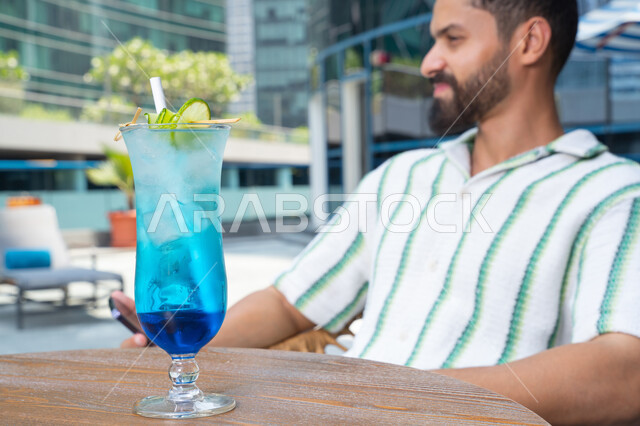 صورة مقربة لعصير بارد منعش, الإستجمام في الهواء الطلق, رجل عربي خليجي اماراتي يرتدي الزي الكاجوال, القيام بالأنشطة الممتعة في الإجازة, أهمية السفر والسياحة وقضاء أيام العطلة, الاستمتاع باجواء هادئه خارج المنزل